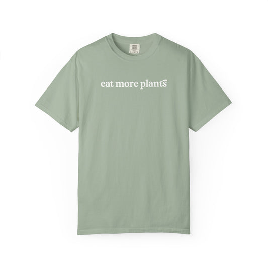Sage green t-shirt with 'eat more plants' text on a white background