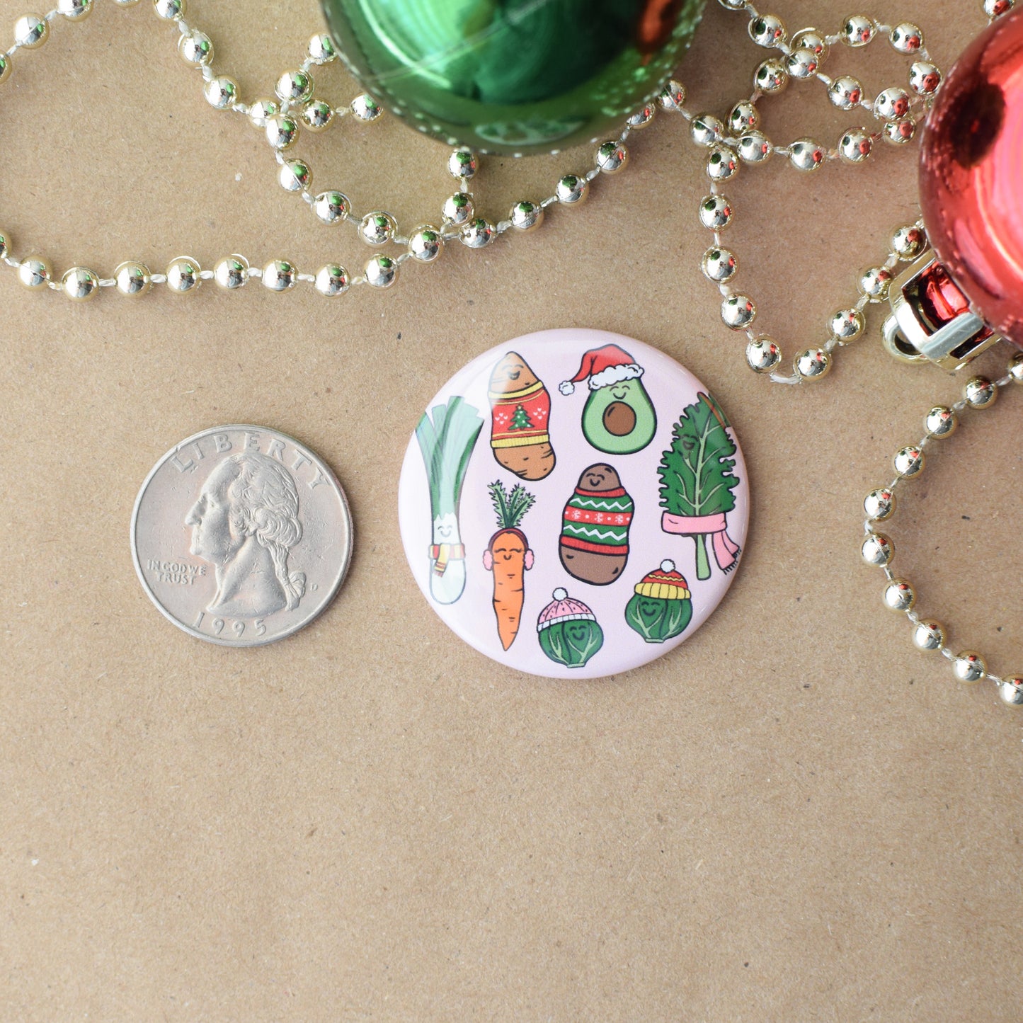 Circular Christmas-themed badge with vegetable illustrations on a brown surface with beads and coins.