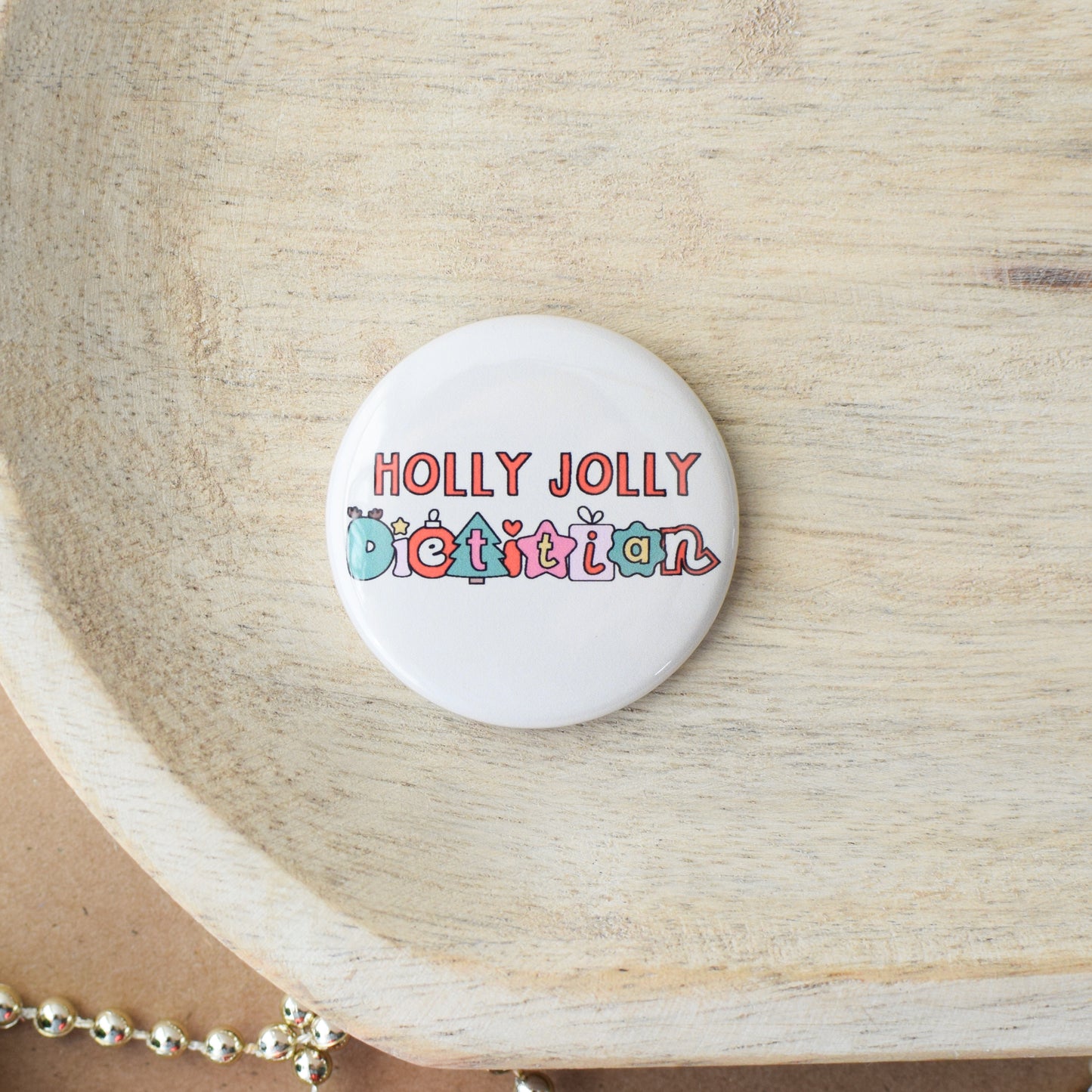 Button badge with 'Holly Jolly Dietitian' text on a wooden surface