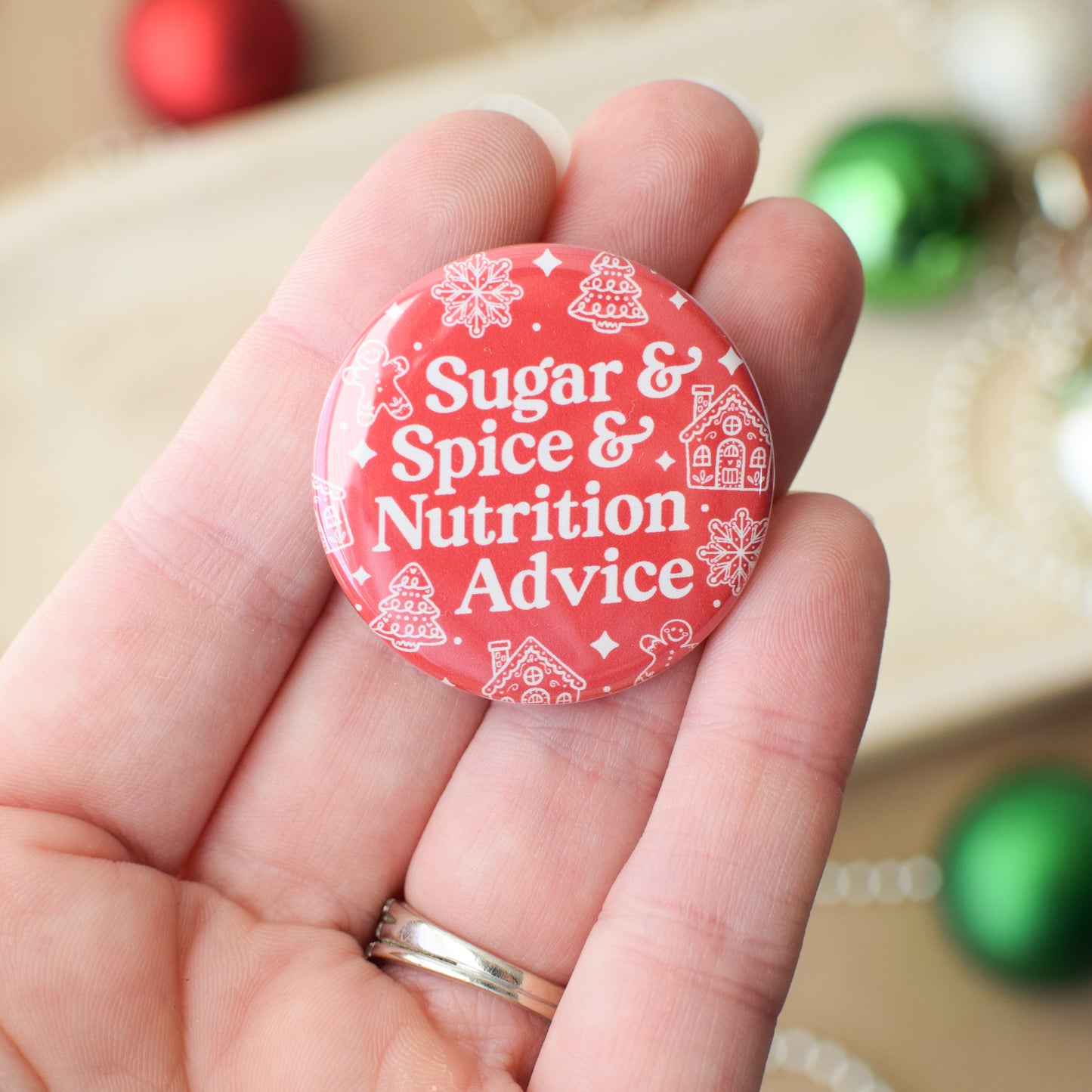 Red button with 'Sugar & Spice & Nutrition Advice' text held in a hand with Christmas decorations in the background.