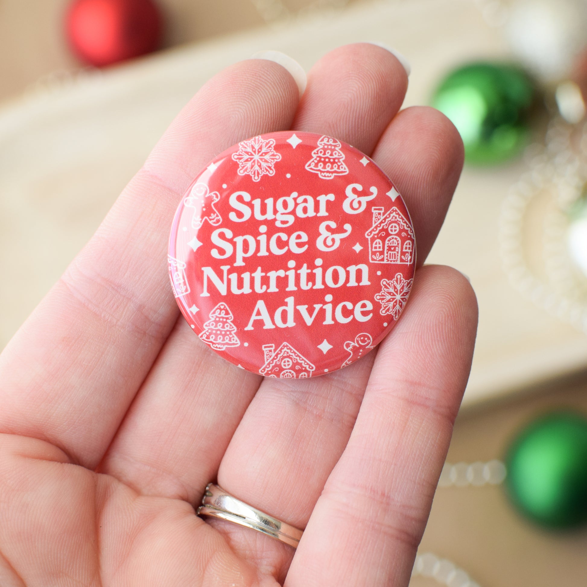 Red button with 'Sugar & Spice & Nutrition Advice' text held in a hand with Christmas decorations in the background.