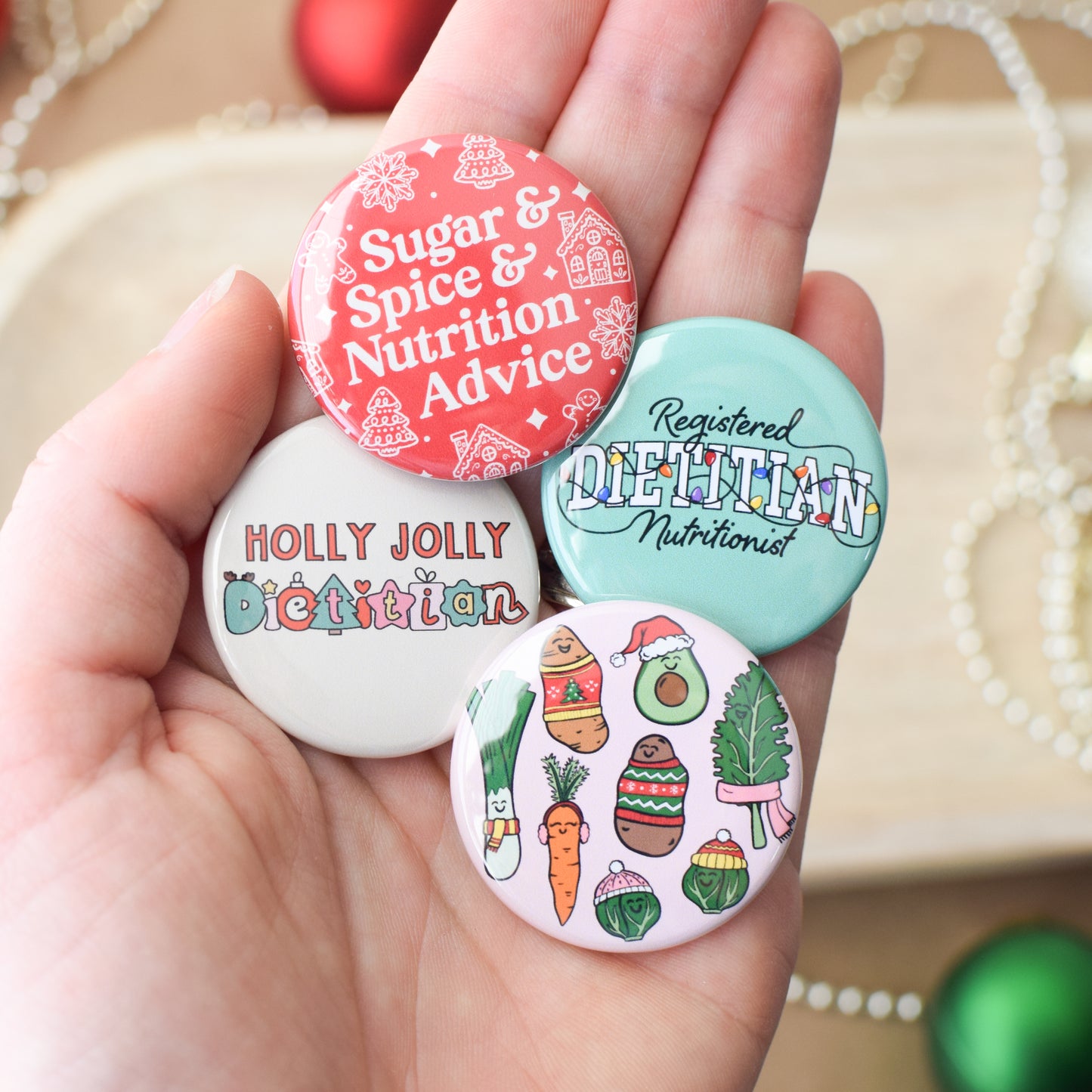 Hand holding four colorful holiday themed buttons with various nutrition and dietitian designs and text.