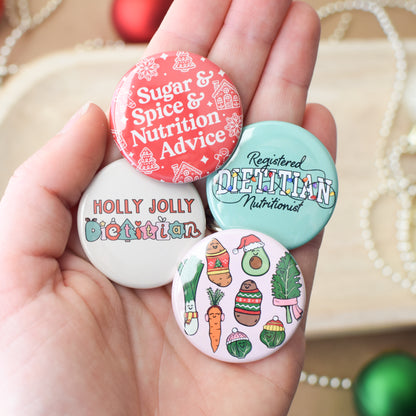 Hand holding four colorful holiday themed buttons with various nutrition and dietitian designs and text.
