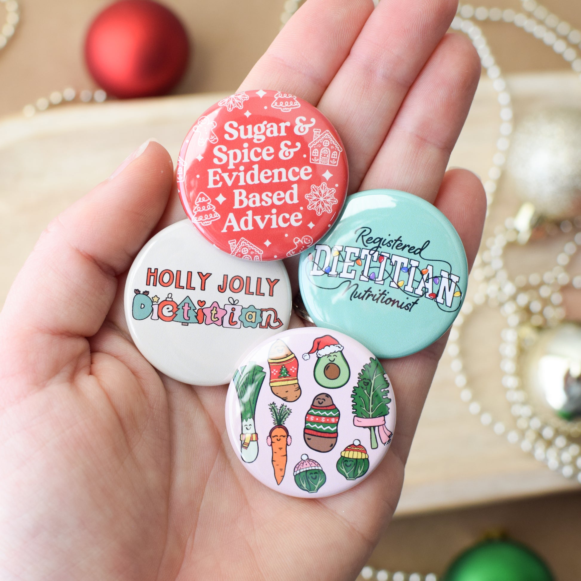 Hand holding four colorful holiday buttons with nutrition and dietitian designs.