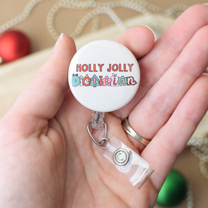 Retractable badge holder with 'Holly Jolly Dietitian' text held in a hand.