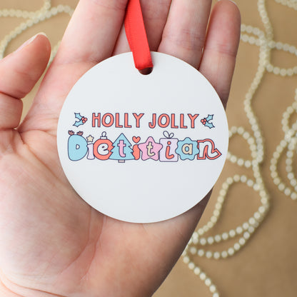 Round off-white ornament with 'Holly Jolly Dietitian' text held in a hand against a beige background.