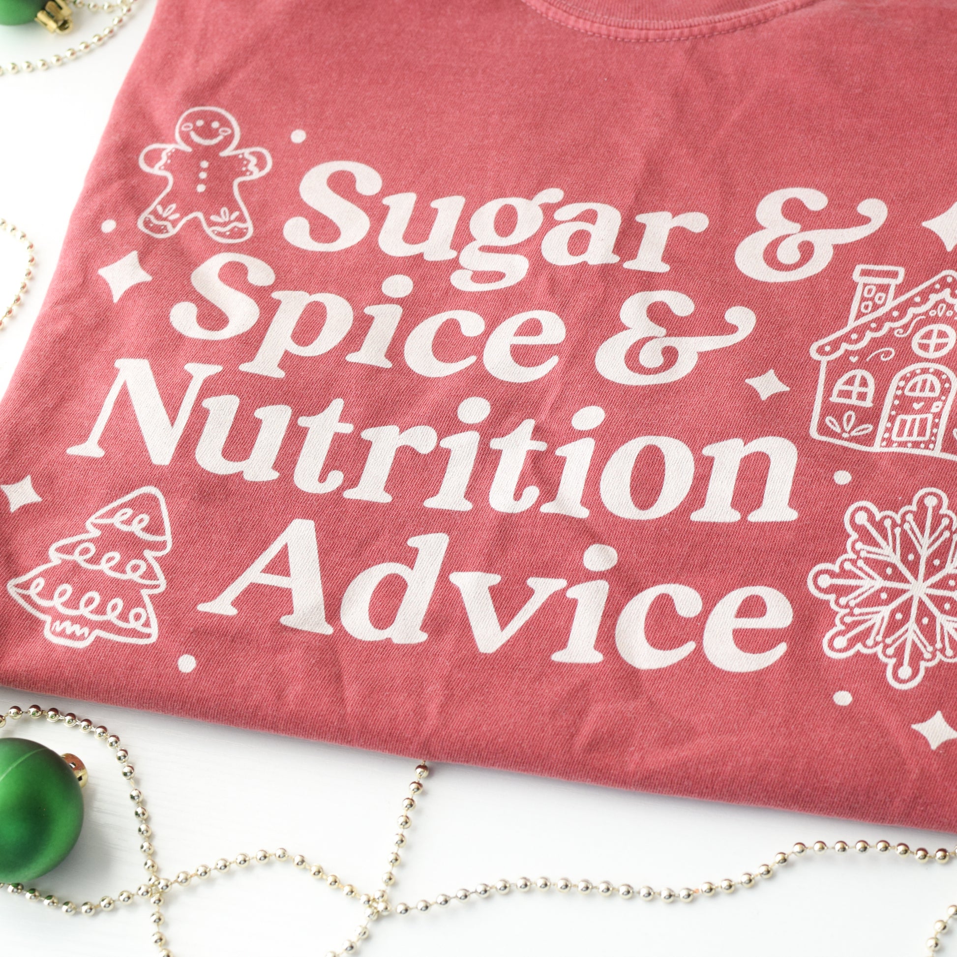 Red t-shirt with white text 'Sugar & Spice & Nutrition Advice' and white gingerbread cookie graphics on a decorative background