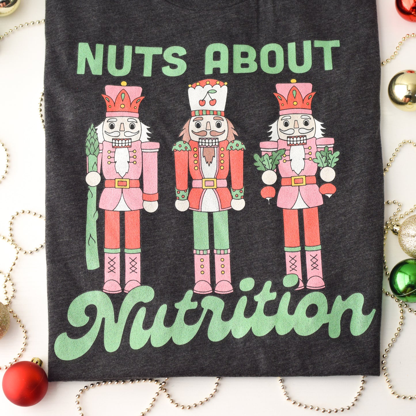 Charcoal t-shirt with nutcracker design and 'Nuts About Nutrition' text, surrounded by Christmas decorations.