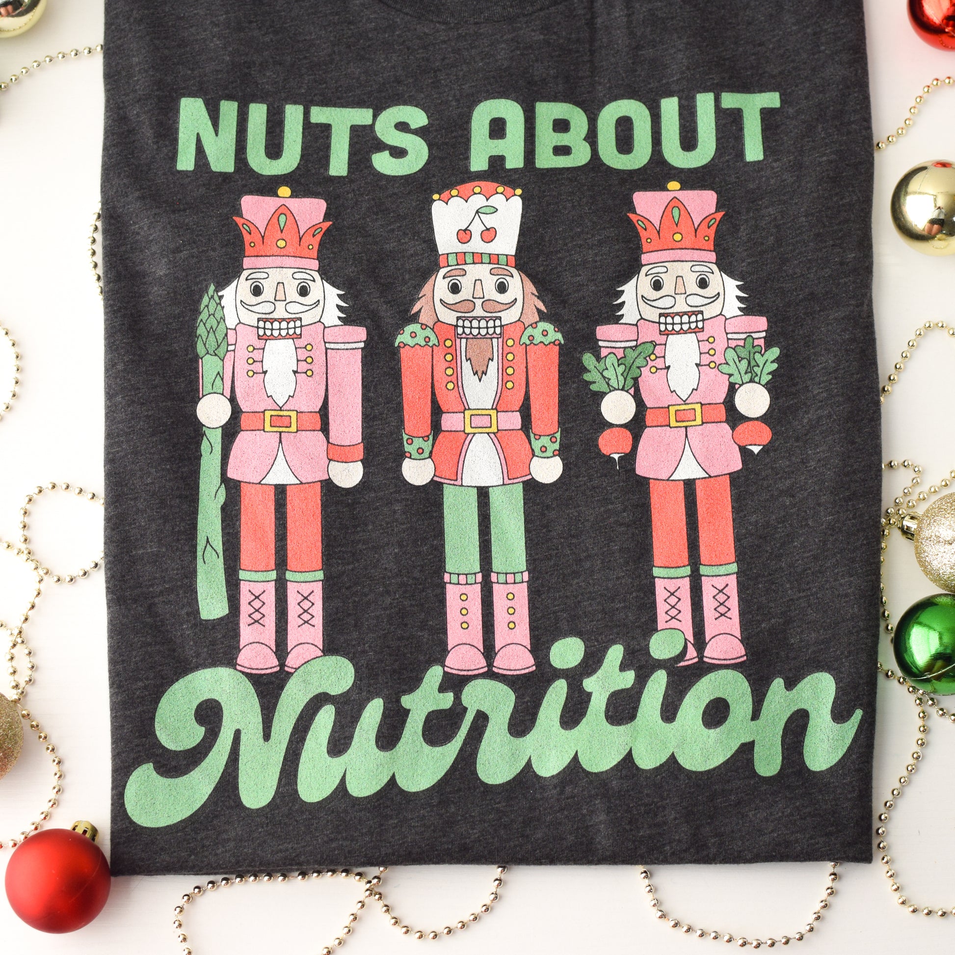 Charcoal t-shirt with nutcracker design and 'Nuts About Nutrition' text, surrounded by Christmas decorations.