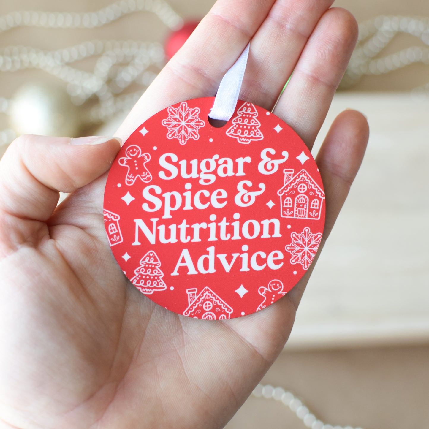 Red circular ornament with 'Sugar & Spice & Nutrition Advice' text held in a hand.