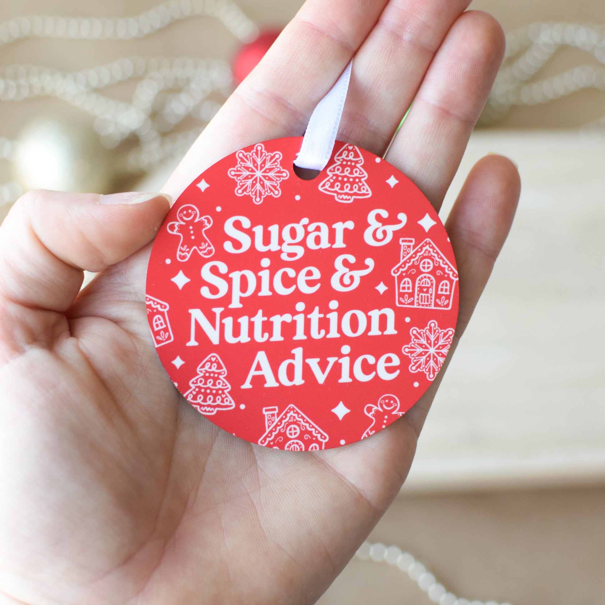 Red circular ornament with 'Sugar & Spice & Nutrition Advice' text held in a hand.