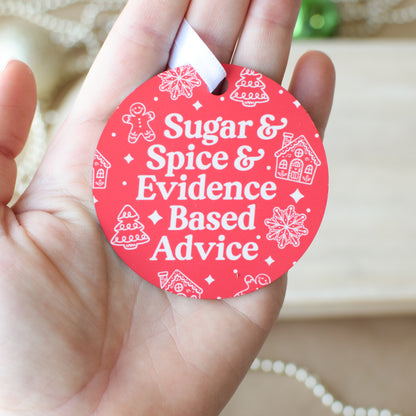 Red circular ornament with white text 'Sugar & Spice & Evidence Based Advice' held in a hand