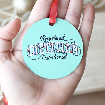 Round green-blue ornament with 'Registered Dietitian Nutritionist' text with Christmas lights held in a hand.