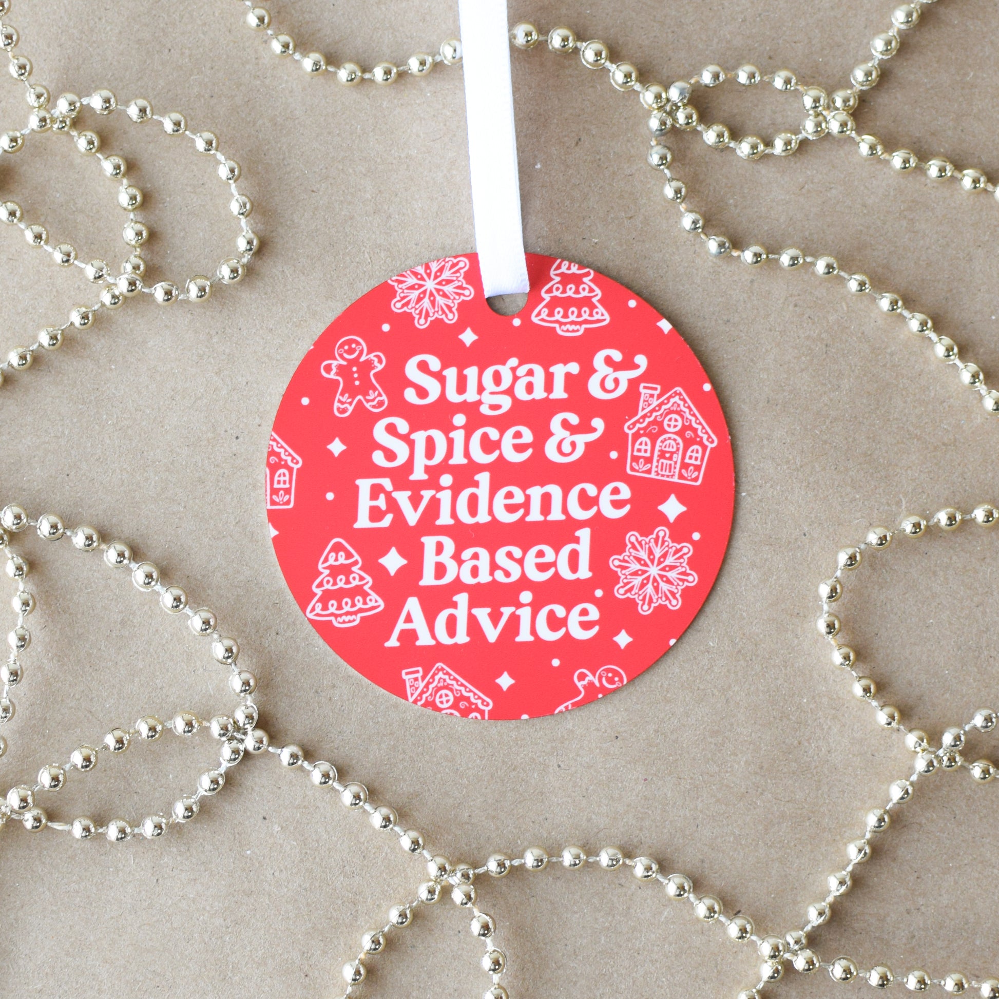 Red circular ornament with text 'Sugar & Spice & Evidence Based Advice' on a beige background with gold beads.