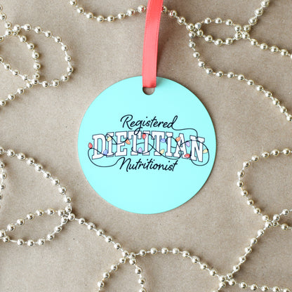 Round green-blue ornament with 'Registered Dietitian Nutritionist' text on a beige background with silver beads.