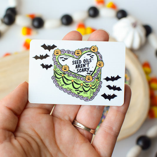 Hand holding a card with Halloween-themed design and text, surrounded by festive decorations.