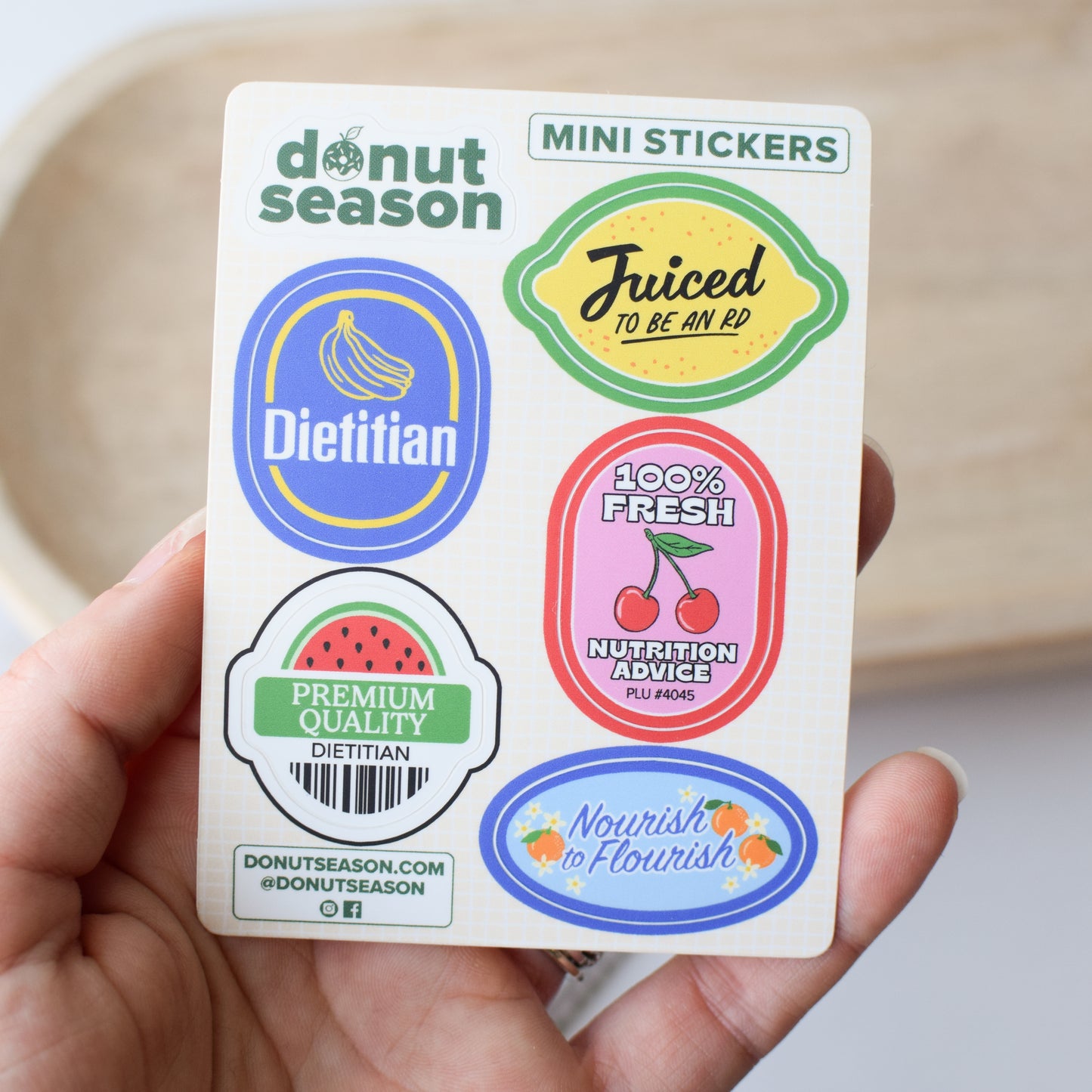 Pack of mini stickers for dietitians with various produce sticker inspired designs held by a hand